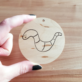 A small plywood disc with a smiling worm engraved onto it
