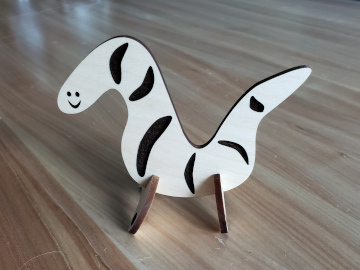 A wormlike creature laser cut from plywood with a smile and two pairs of legs.