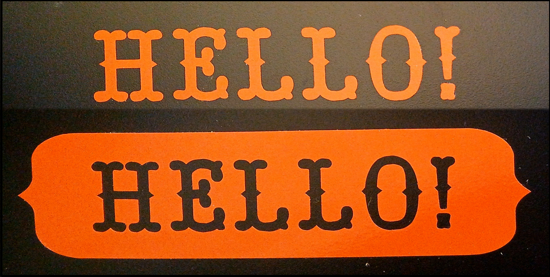 Two hellos cut from vinyl and applied to a black surface. The first hello is just the letters in orange vinyl. The second hello has the letters removed from a larger piece of vinyl which has been applied to the surface.