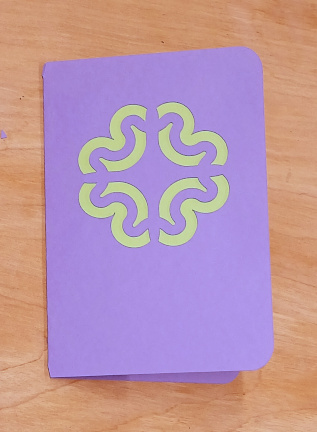 A purple card that has a design cut into it to reveal a green interior.