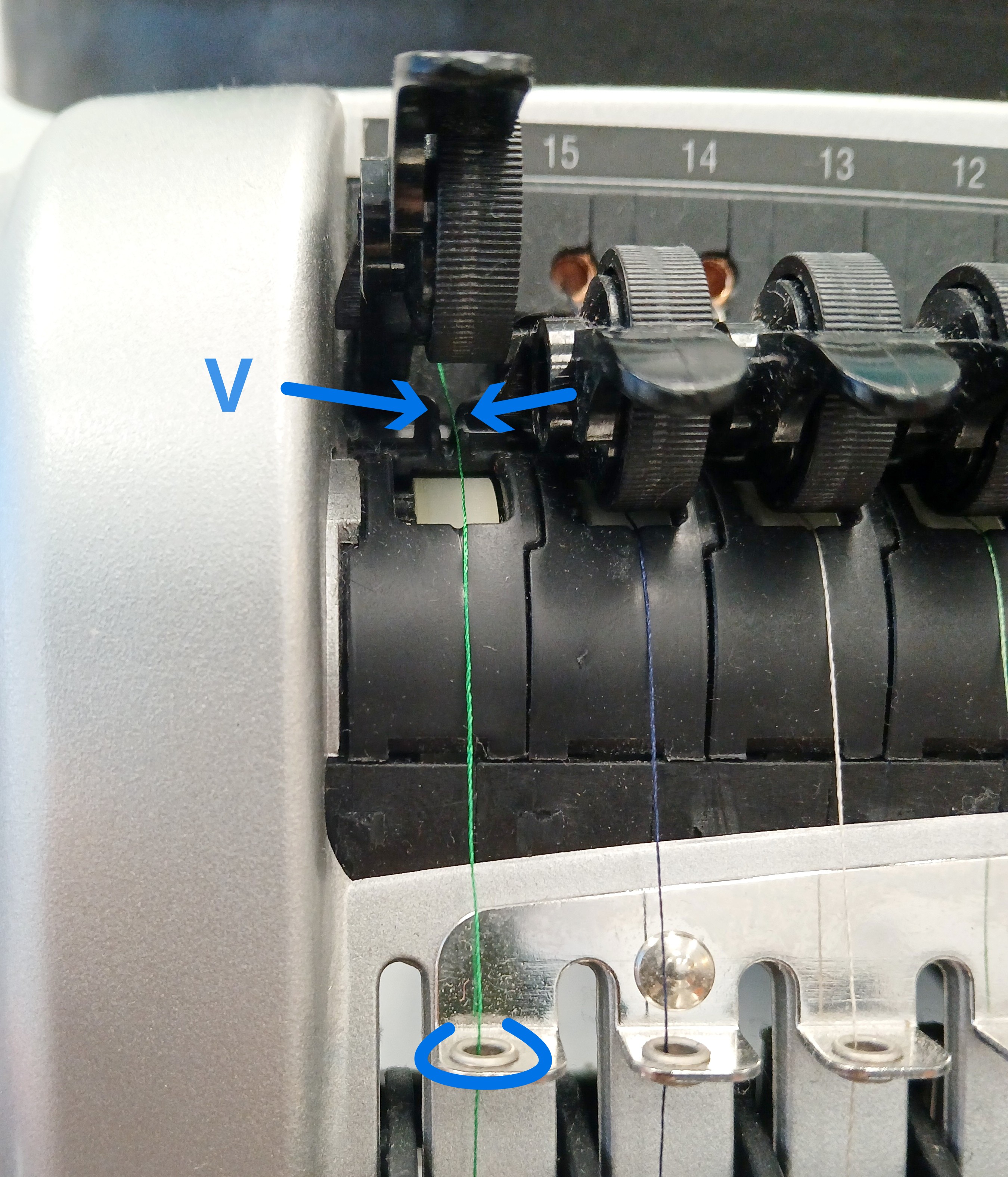 A thread appears from behind the tension wheel, passing through a black plastic V shape that is hidden behind the wheel before continuing down the front of the machine.