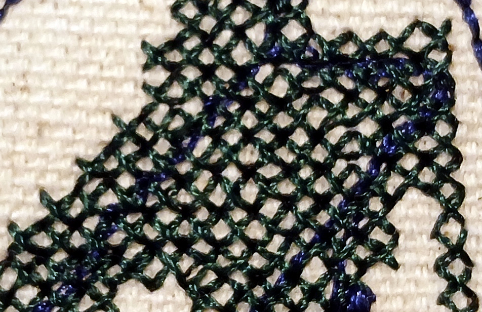 An irregular shape resembling a human torso is filled with X shaped stitches. The shape does not have an outline. A line of running stitch is visible underneath the X stitches.